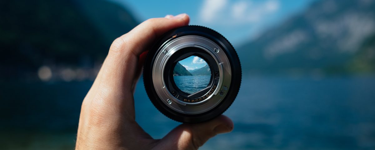 man holding up camera lens to see landscape in focus